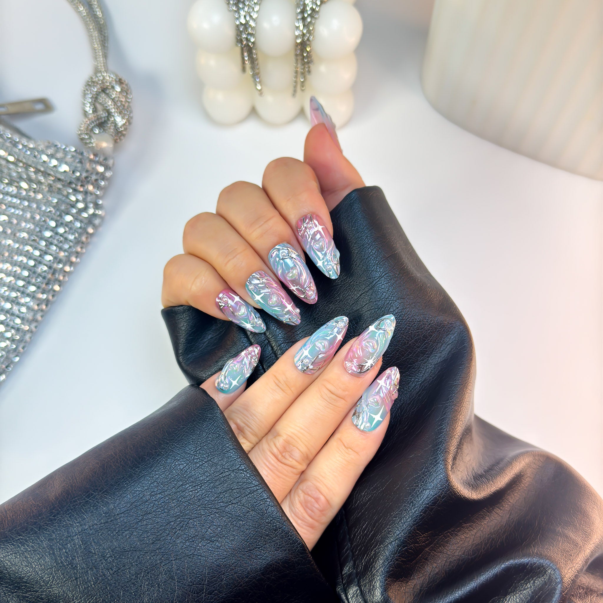 Cosmic press-on nails with holographic chrome gradient from soft pink to blue, captured in an angled hand pose for shine and detail.