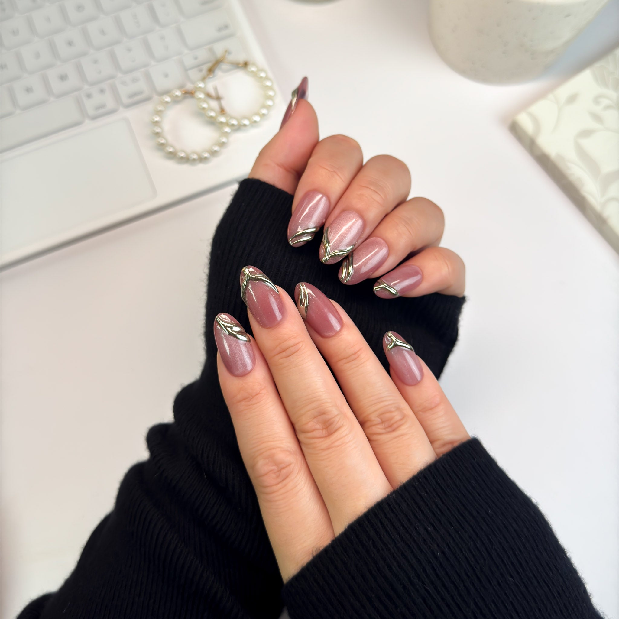 Gilded Strike nails in angled pose — deep rose tones paired with gleaming gold accents, creating a sophisticated molten-metal effect.