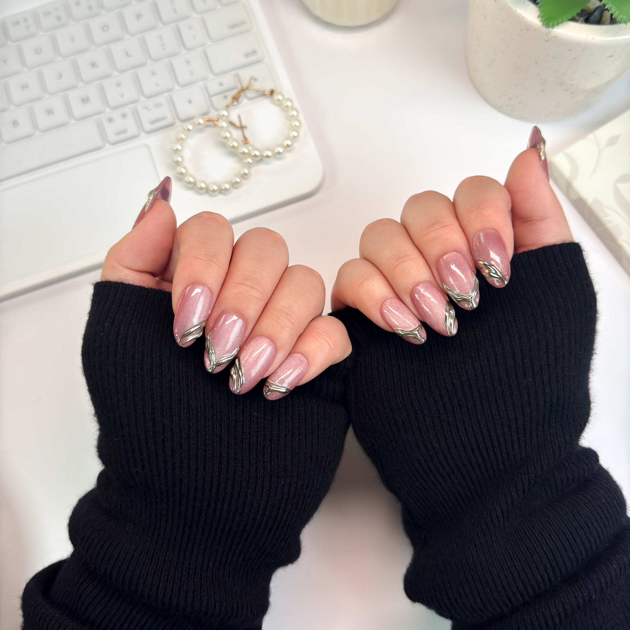 Gilded Strike nails styled with cozy black sleeves — a mix of shine and shadow, featuring metallic gold strokes on mauve bases.