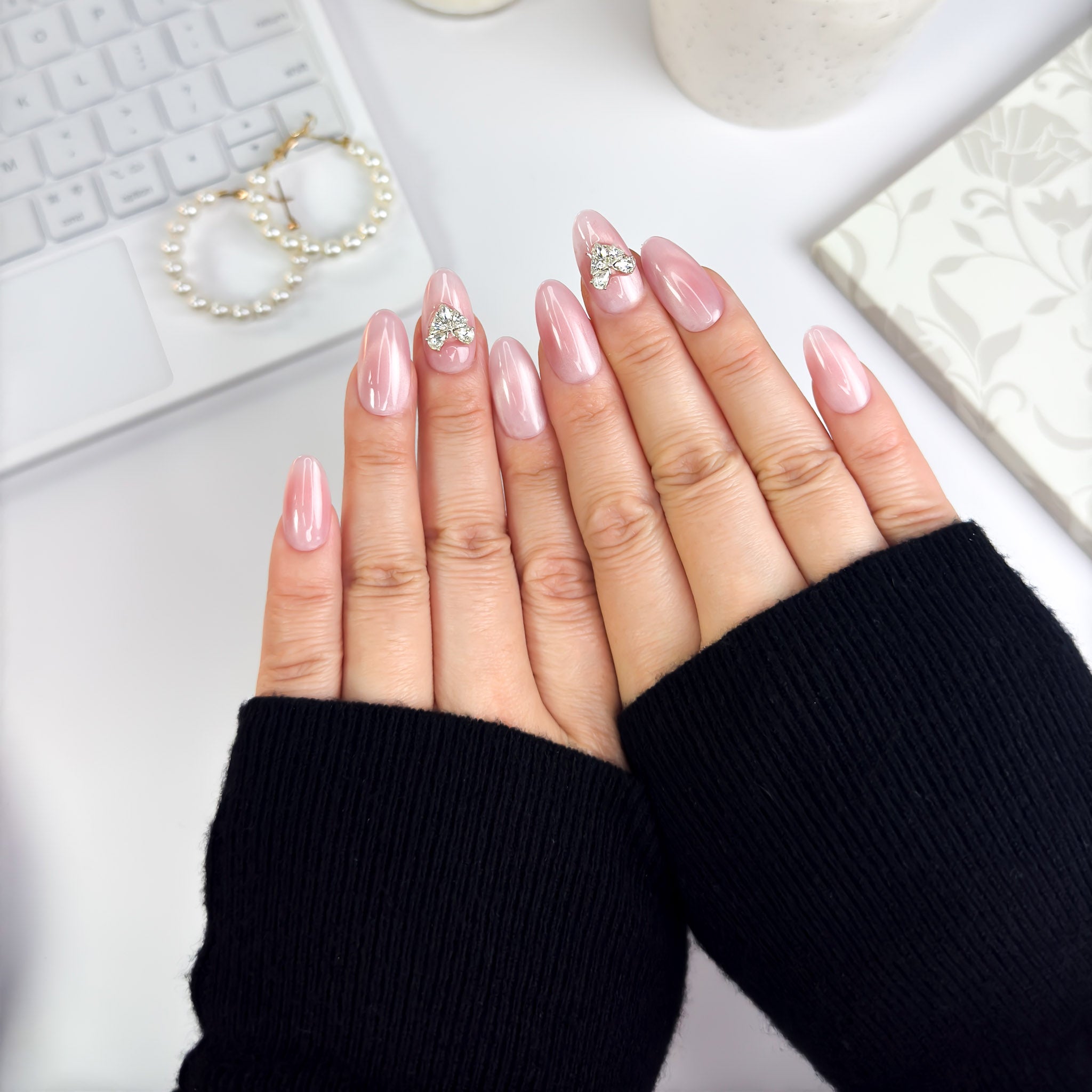 Flatlay of Magnetic Love nails — romantic pink tones with heart-shaped crystal accents, worn in a cozy, elegant setting.