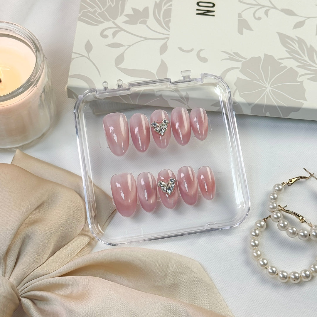 Magnetic Love press-on nails — soft pink hue with crystal heart embellishment, styled with neutral tones, candlelight, and pearls for an elegant aesthetic.