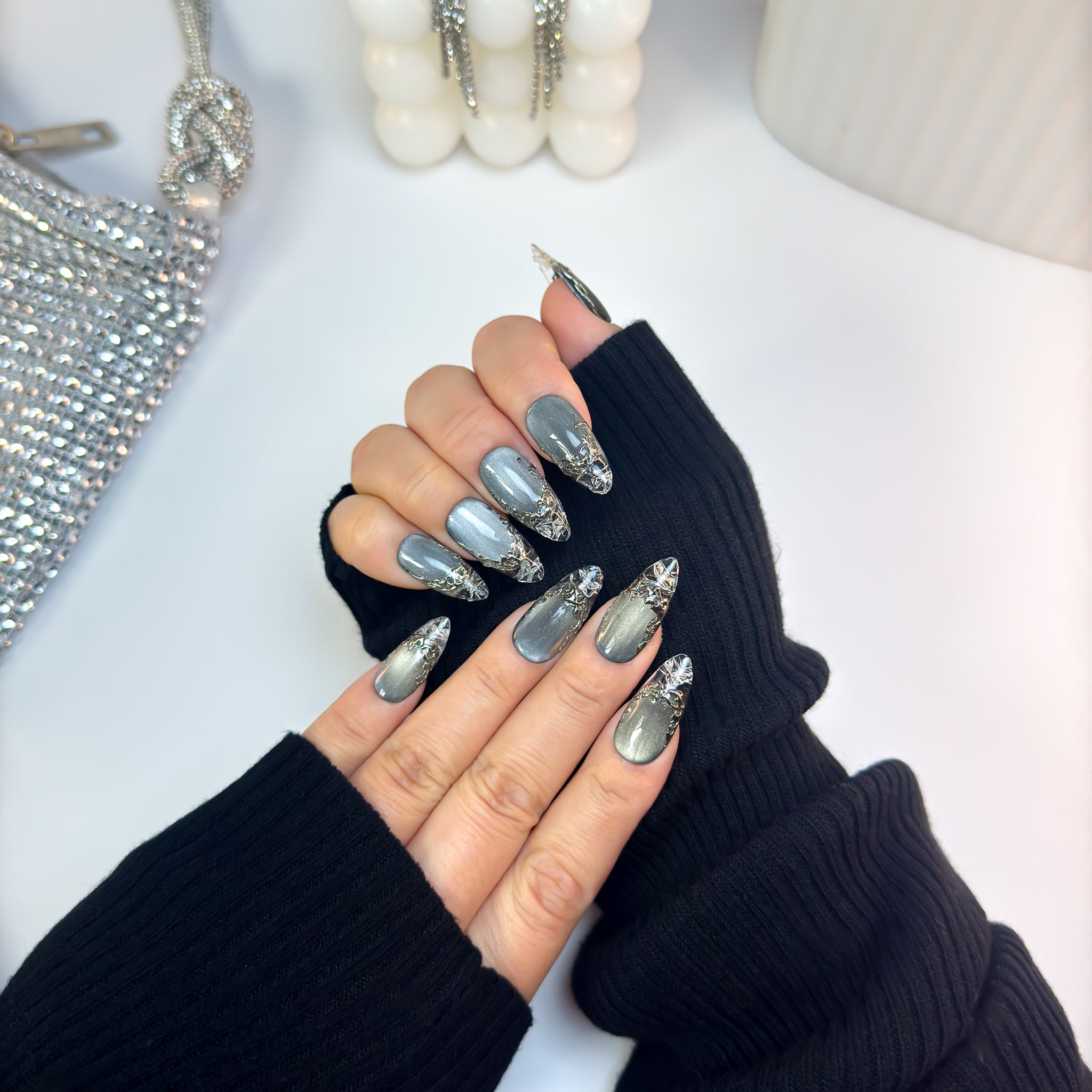 Molten Glass nails with reflective steel tones and molten silver drip design, captured in an angled hand pose to highlight the glass-like shine.
