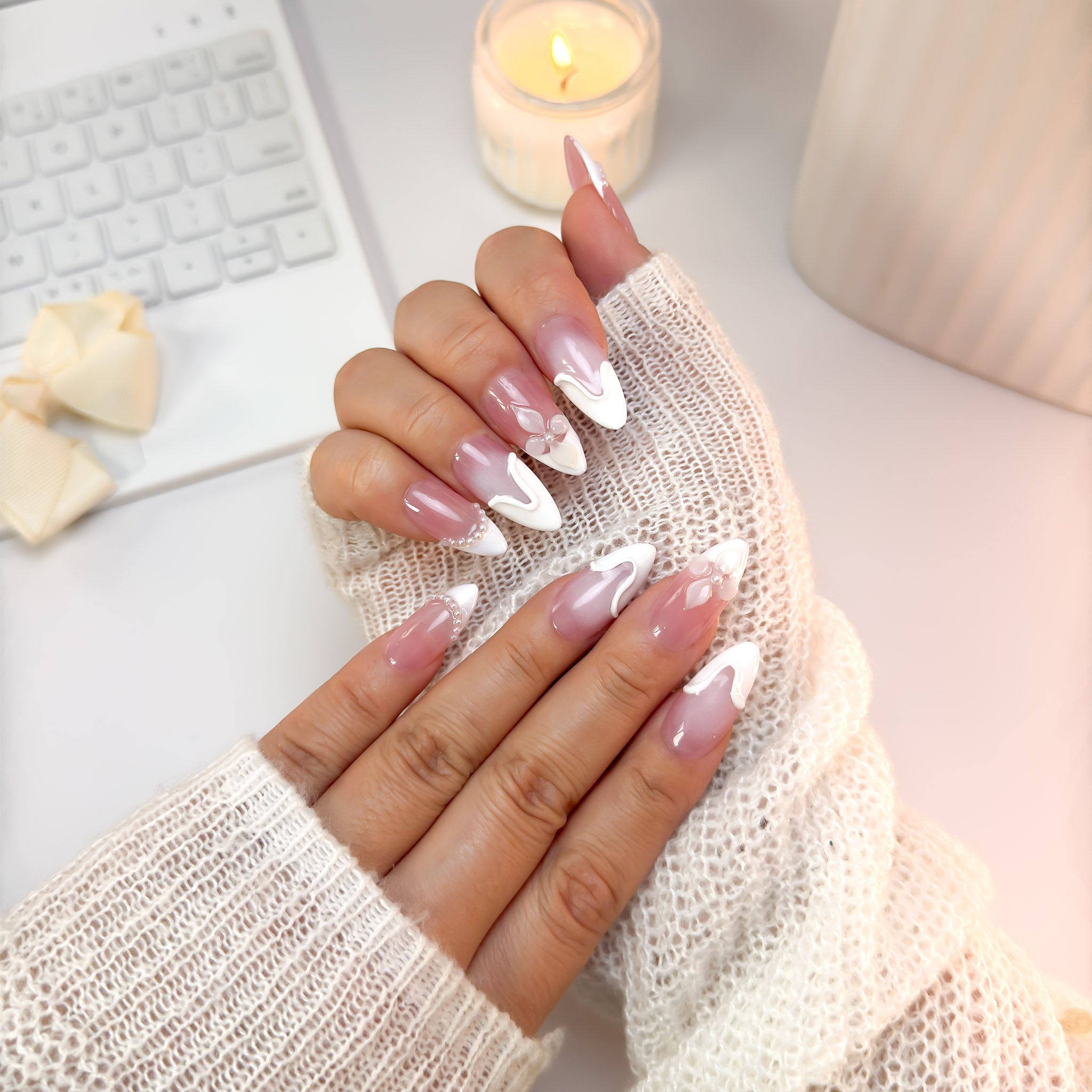 Soft Serve press-on nails in soft candlelight — creamy blush tones with sculpted white swirls and petal accents, paired with a cozy knit sweater for a warm, elegant glow.