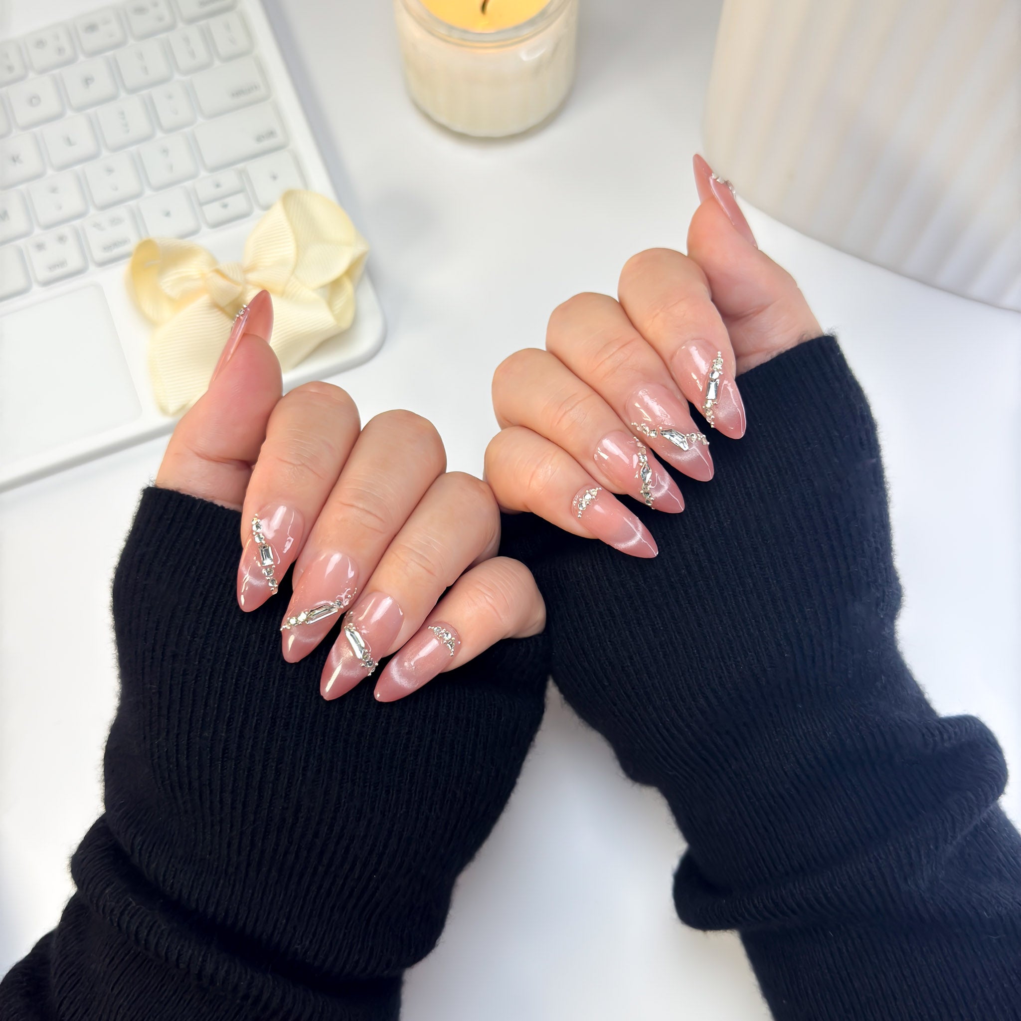 Sunlit press-on nails with luminous peach-pink sheen and minimalist shine, shown in a soft, sunlit hand pose wearing black ribbed sleeves.