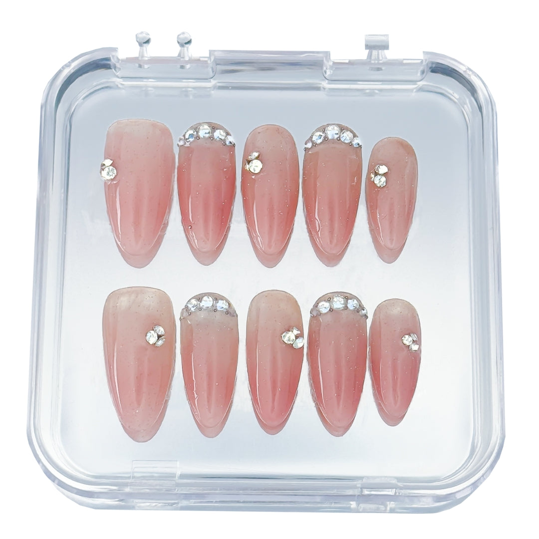 Twinkle Touch press-on nails by Lunoxcore — a soft nude-pink base with subtle shimmer and crystal accents, presented in a clear display case for a refined, luminous look.