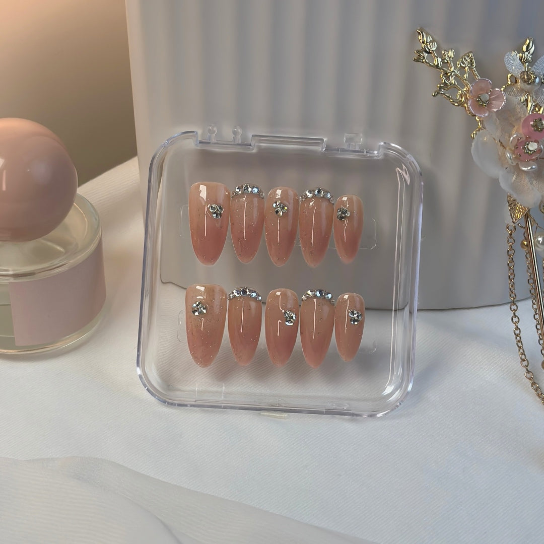 Twinkle Touch press-on nails by Lunoxcore — a soft nude-pink base with subtle shimmer and crystal accents, presented in a clear display case for a refined, luminous look.