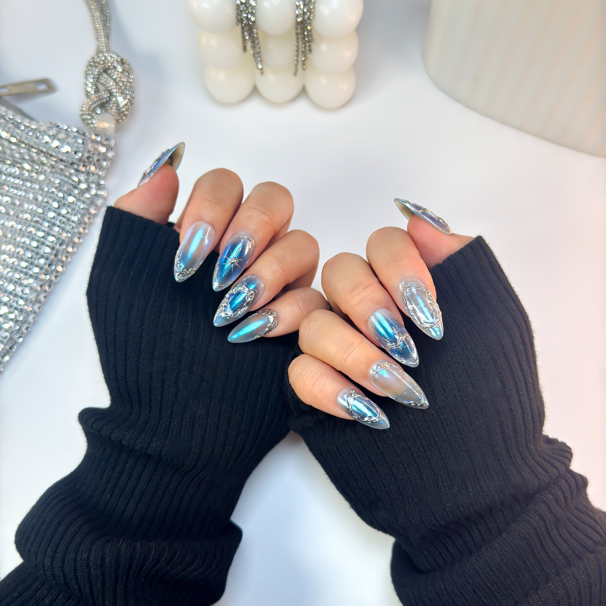 Metallic blue chrome Voltage press-on nails with raised silver detailing, shown on both hands in a forward pose.