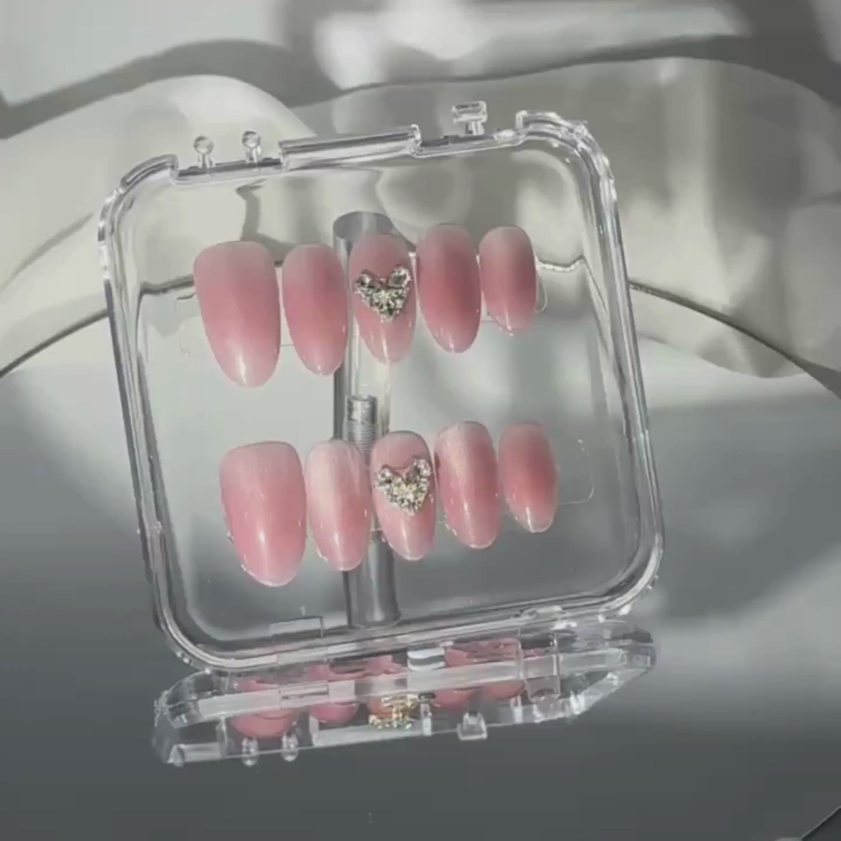 Soft-lit shot of Magnetic Love nails highlighting their crystal heart centerpiece and subtle pink shimmer for a romantic, polished look.